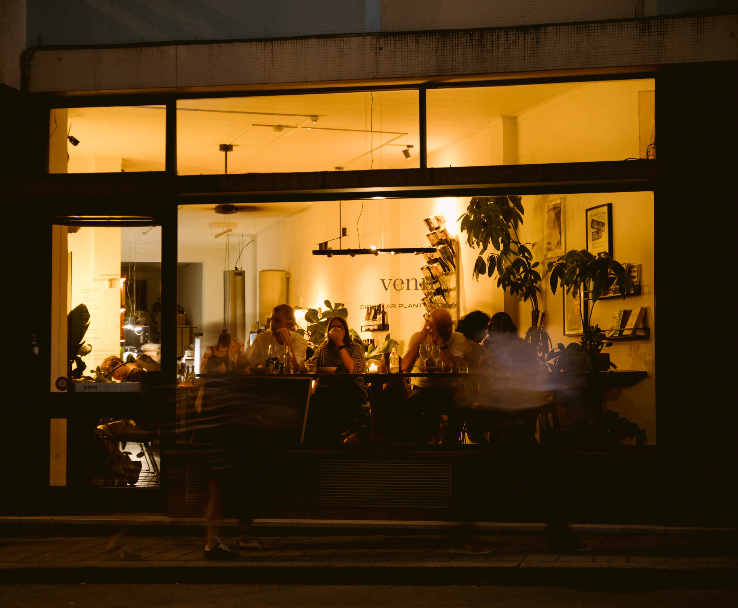 a venn vista da rua à noite, com pessoas a jantar atrás da montra iluminada