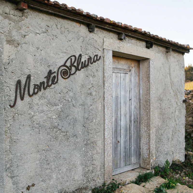 uma pequena casa de pedra com Monte Bluna escrito em ferro na parede